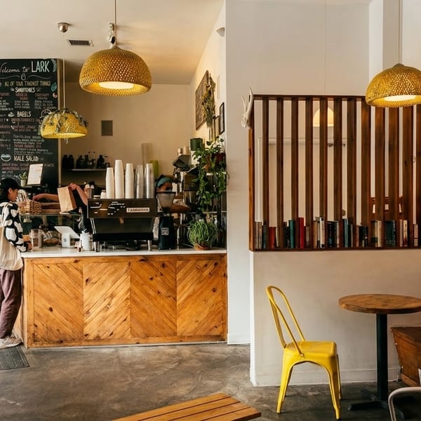 Customers ordering at a bright, modern cafe with wooden accents, yellow chairs, and a chalkboard menu.