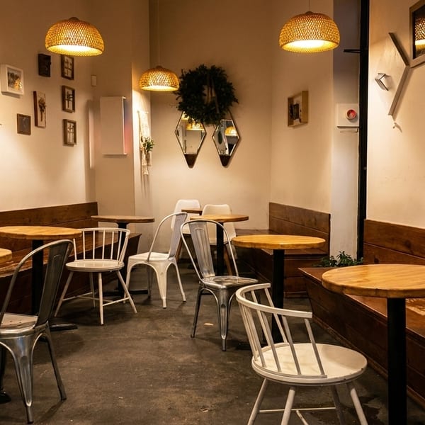 Cozy cafe interior with wooden benches, round tables, and eclectic framed art on light walls.