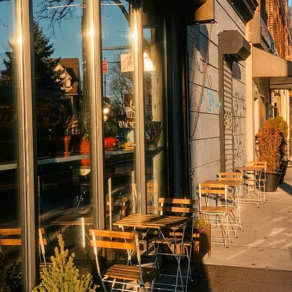 Sunny street view of a restaurant storefront with outdoor seating and reflections in the windows.